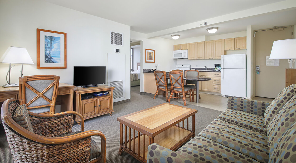 Living room with a couch, coffee table, desk, TV, and entry to kitchen.
