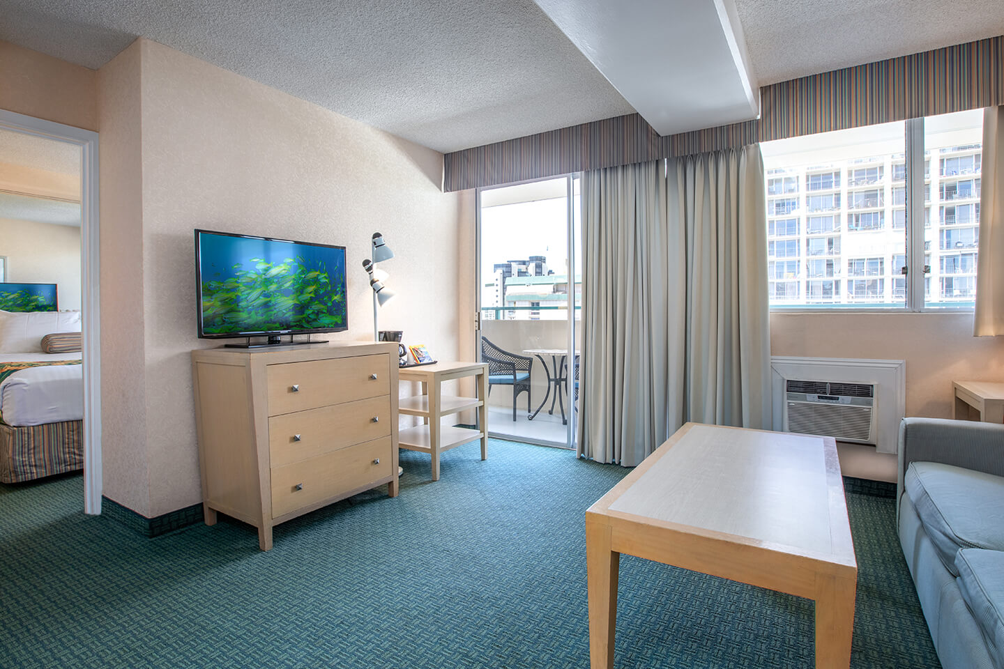 Living area with TV on dresser, coffee table, couch, and balcony.