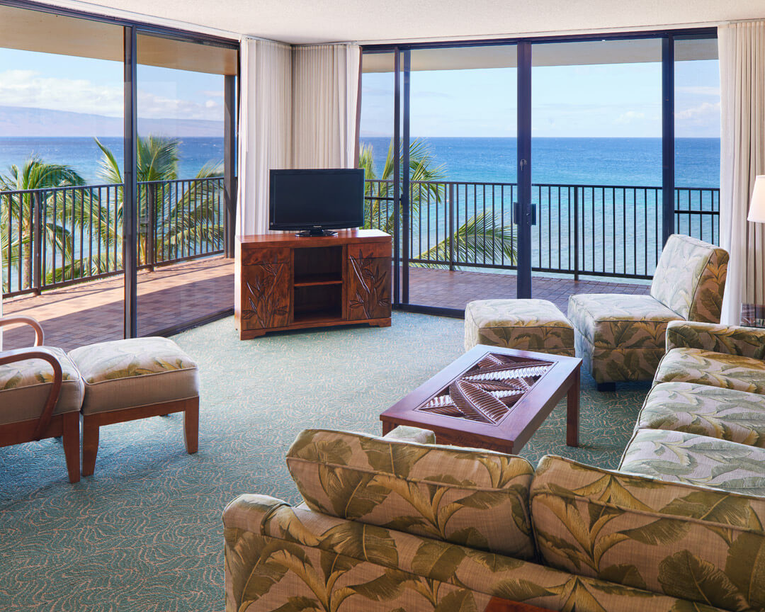 Room with living space, sitting area, and balcony with ocean view.