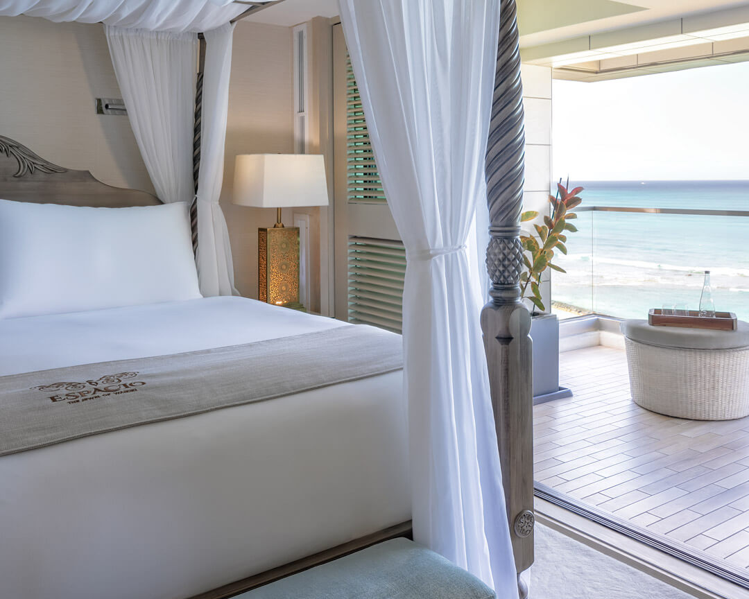 Master bedroom with four-poster bed and sliding door opening to balcony overlooking the ocean.