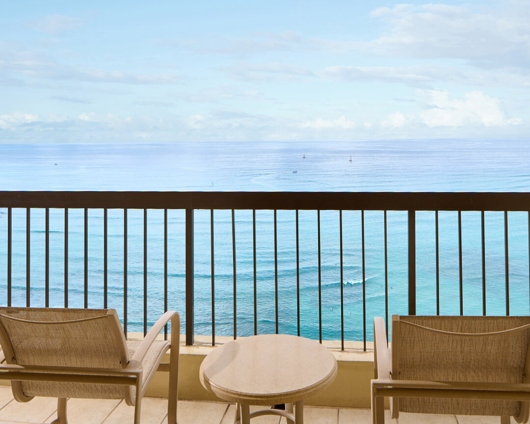 Two chairs and small table on balcony overlooking the ocean.