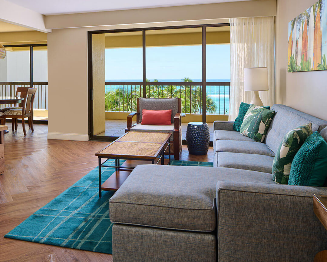 Living area with a couch, coffee table, TV, and balcony with ocean view.