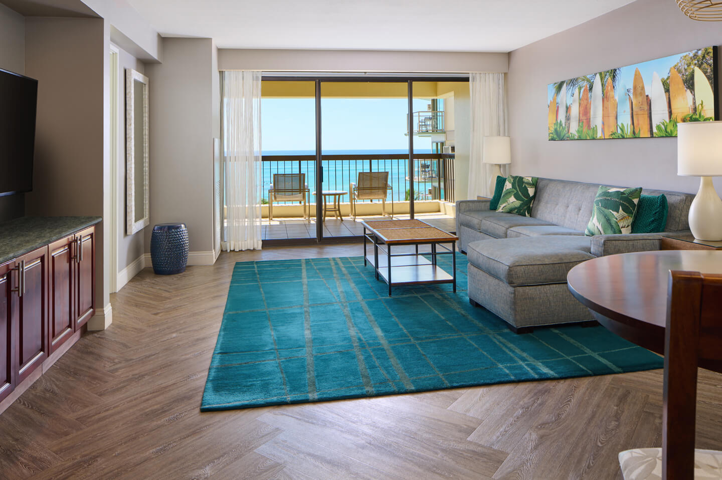 Living area with couch, coffee table, dining area, TV, balcony with ocean view.