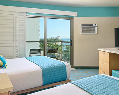 Room with 2 beds, nightstand, lamp, TV, and balcony.