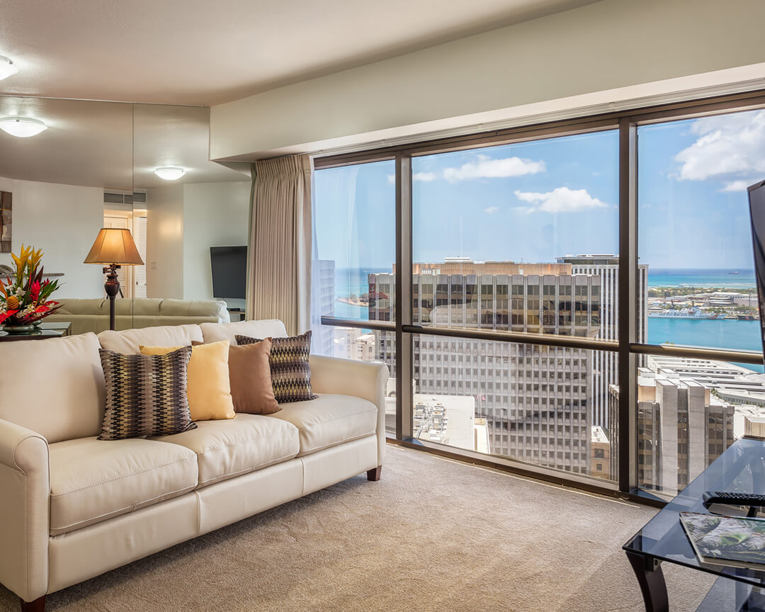 Room with a sofa, and large picture windows with city and ocean views.