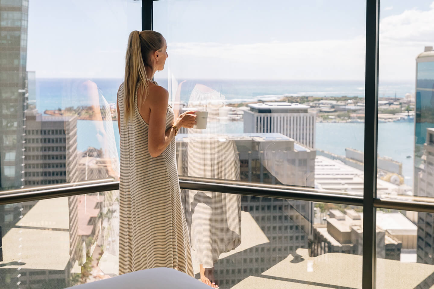Woman drinking coffee and gazing at view from large picture window.