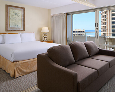 Room with a bed, desk, TV, lamp, and balcony.