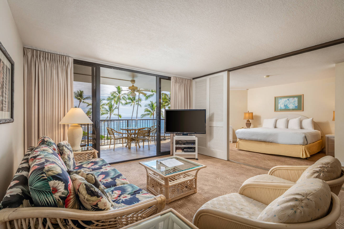 Living area with a couch, coffee table, TV, entryway to bedroom, and balcony with ocean view.