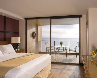 Room with a bed, lamp, and balcony with ocean view.