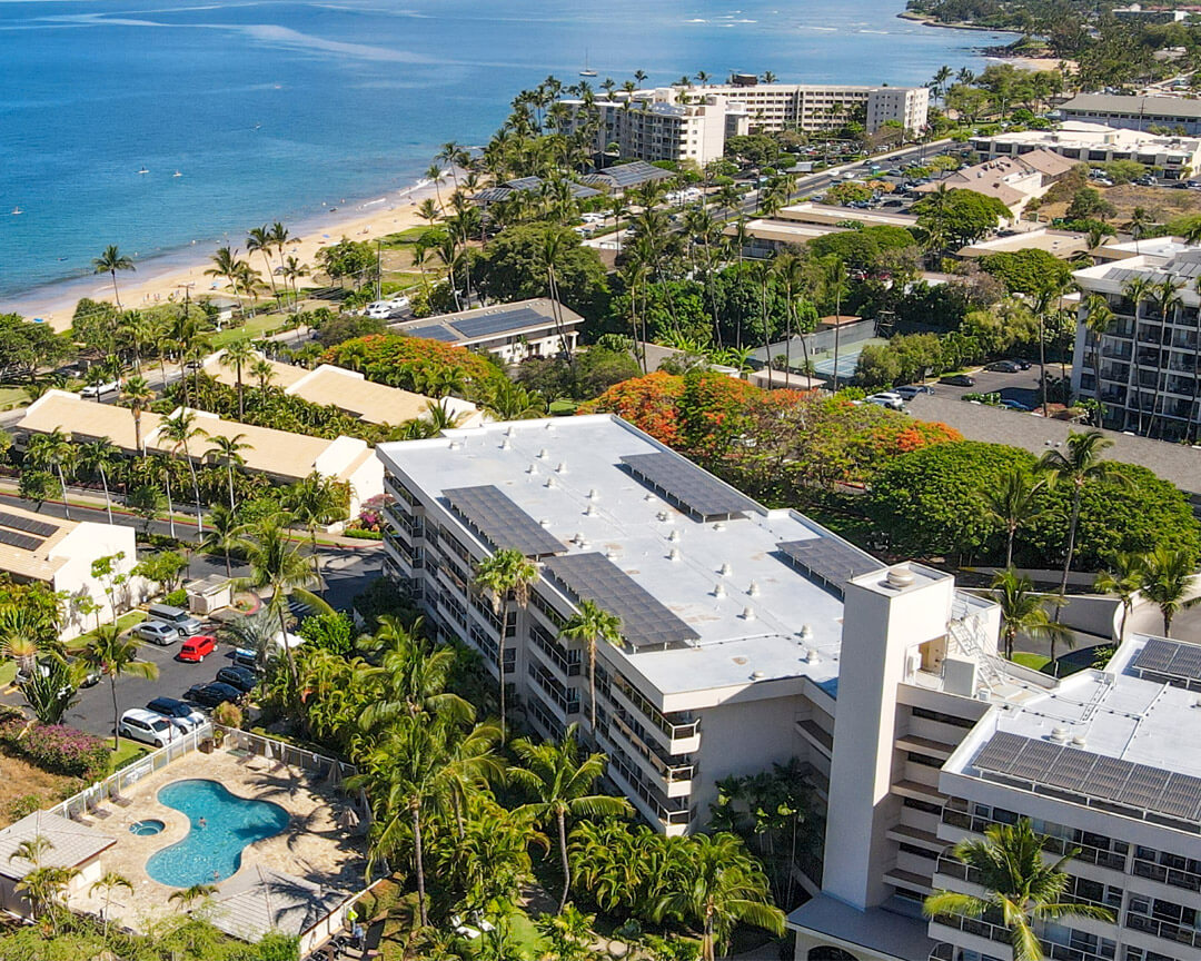 Overhead view of resort with pool, building, tropical lanscape, with ocean and mountain views in background.
