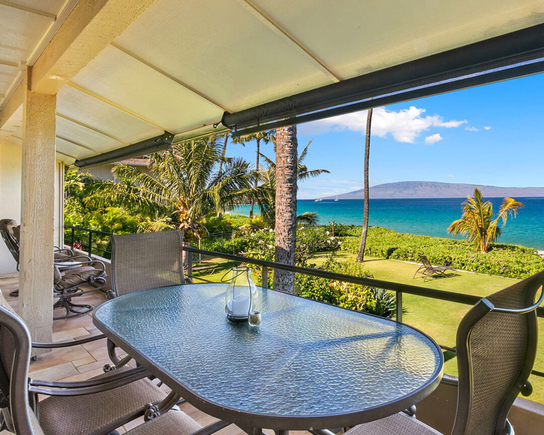 Patio with large table and four chairs, overlooking the ocean.