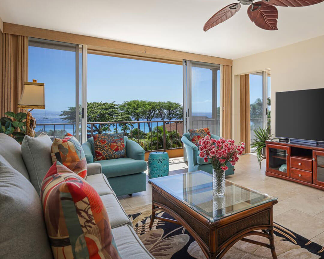Living area with couch, table, balcony overlooking the ocean.