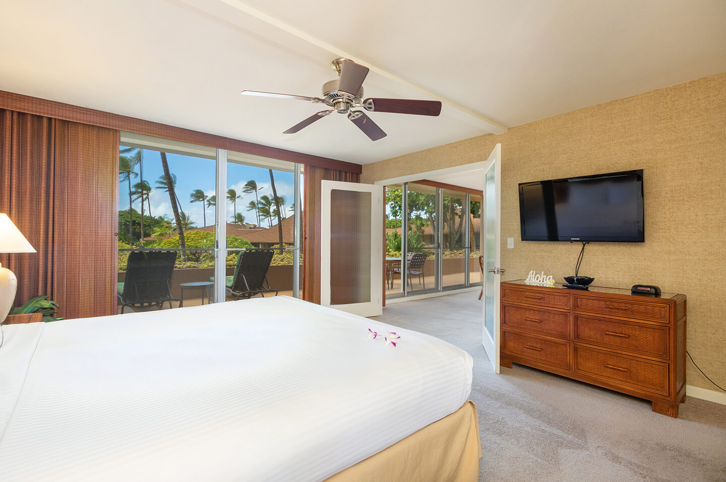 Room with a bed, TV, dresser, and balcony.