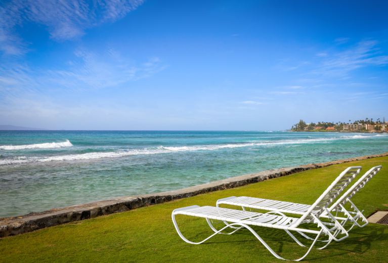 Lounge chairs on the grassy area near the shoreline at Aston at Papakea Resort