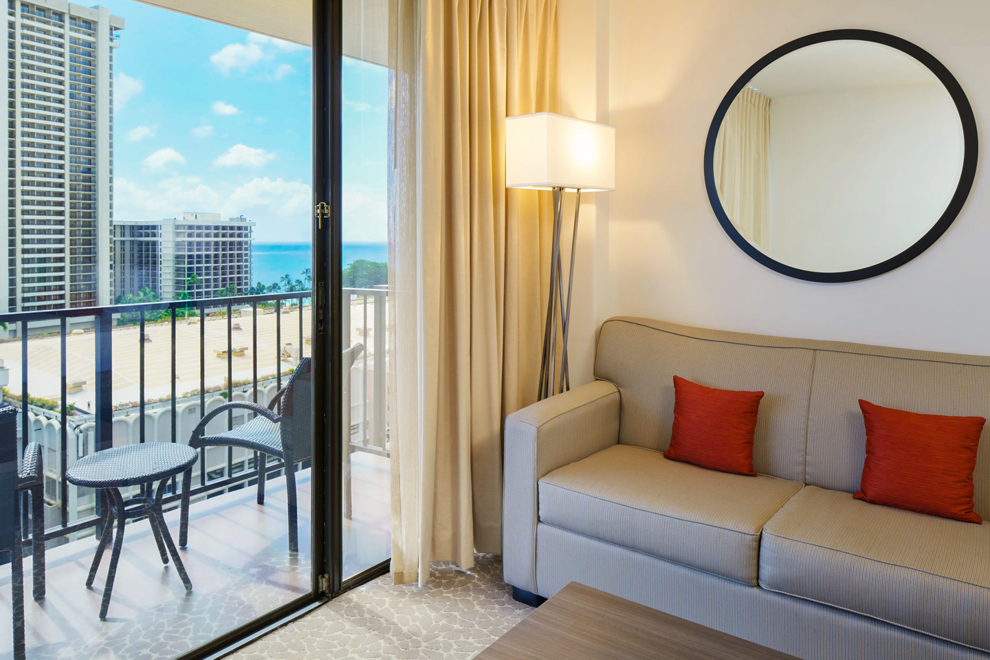 Room with couch, balcony with table and chairs, view of ocean in distance.