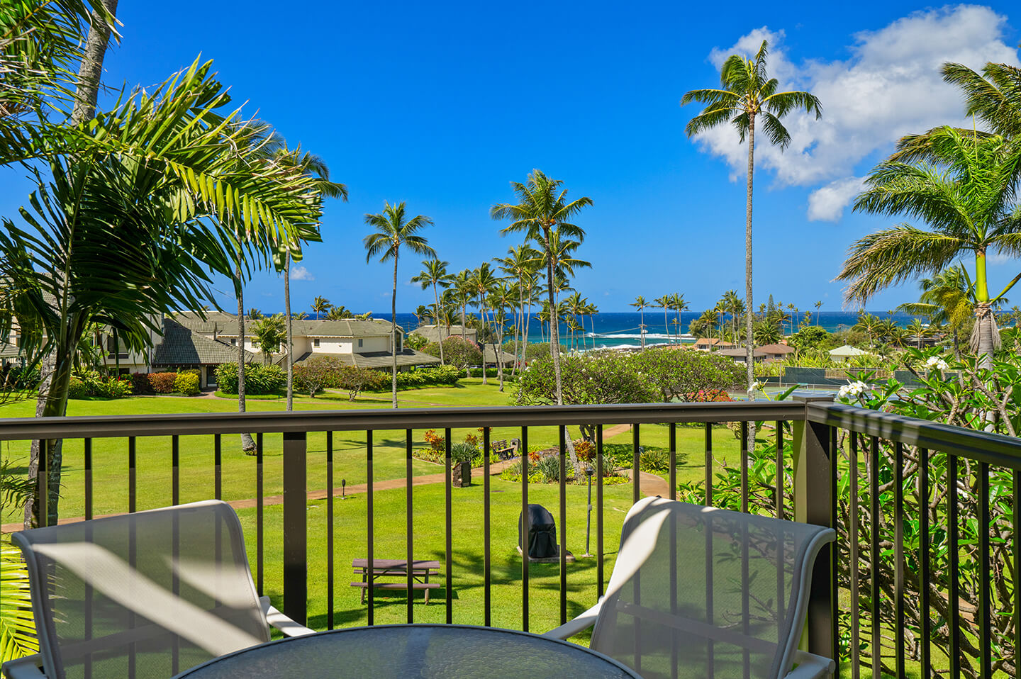 Balcony with table and chairs with garden and ocean view.