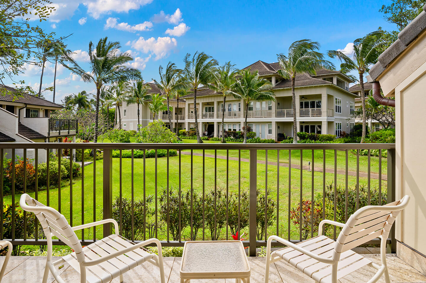 Balcony with table, chairs, and view of resort gardens and ocean.
