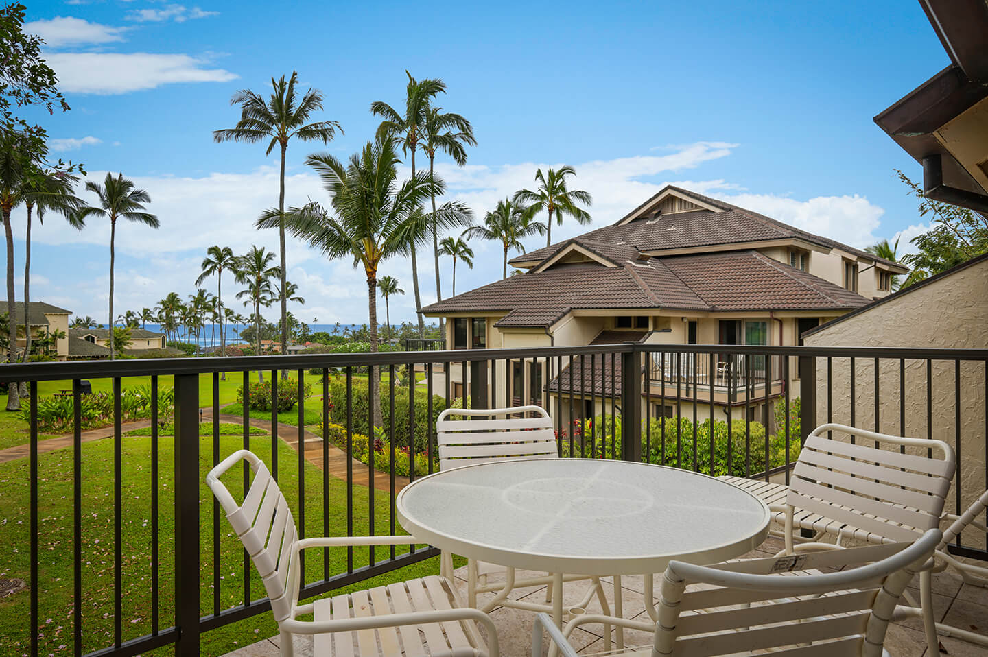 Balcony with table, chairs, and view of resort gardens and ocean.