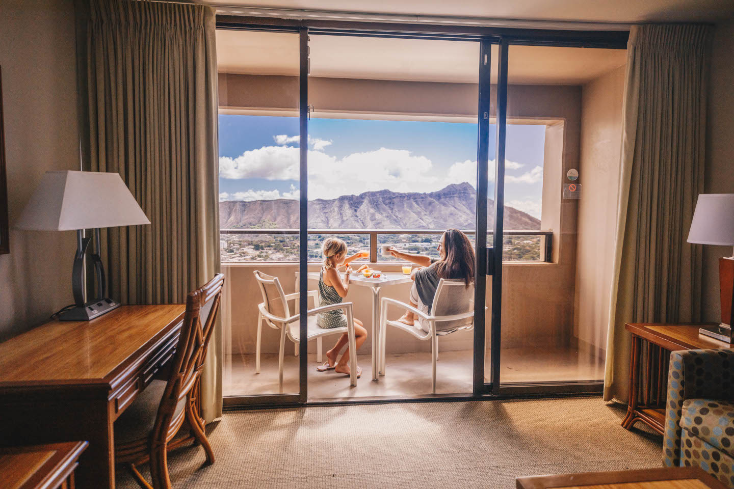 Lady and young girl sitting on balcony enjoying meal looking at views.