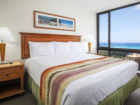 Room with bed, nightstand, lamp, large window with ocean view 