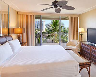 Room with a bed, dresser, TV, chair, lamp, and balcony.